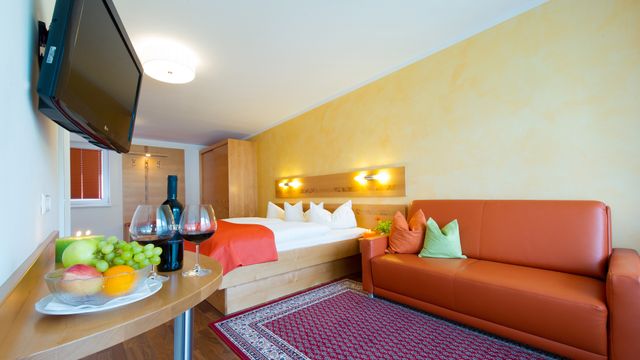 Zimmer mit Couch, TV, Tisch und Doppelbett